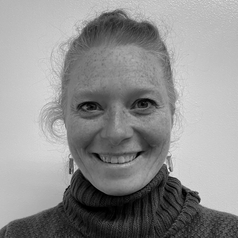 A Ballet Vermont company dancer smiles at the camera for her headshot. She wears her light hair in a bun and a knit turtleneck.